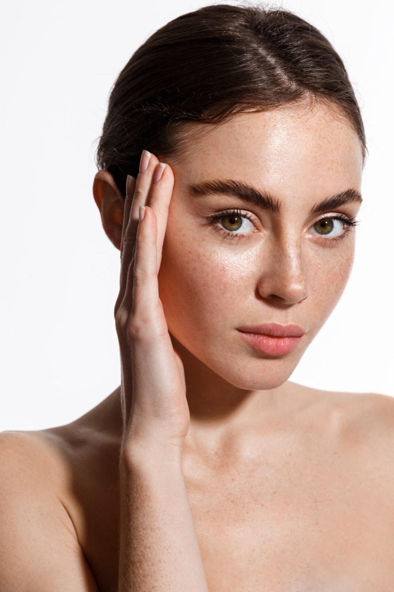 Portrait of young brunette woman with freckles touching her face